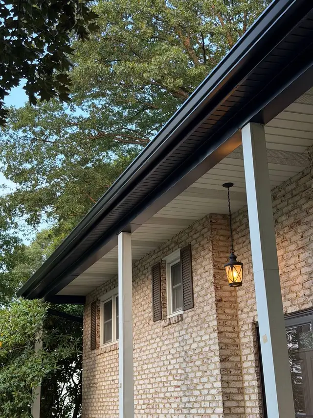 Black seamless gutter along a covered porch roofline on a brick home in Pennsylvania